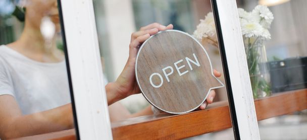Eine Mensch bringt ein Schild hinter einer Glasscheibe an. Auf dem Schild steht "OPEN".