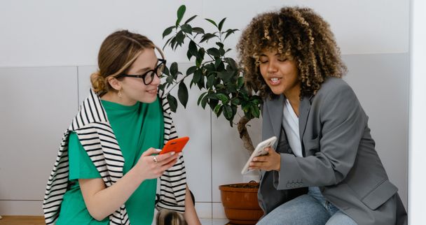 Zwei Frauen sitzen nebeneinander und schauen gemeinsam in das Smartphone der einen.
